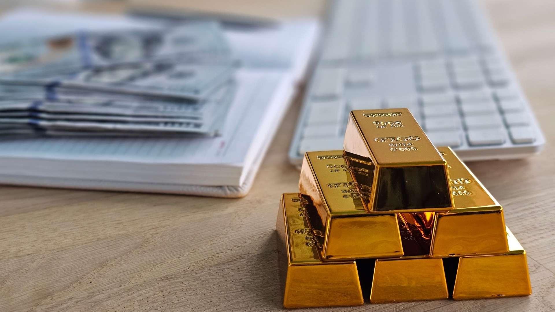 Gold bars and banknotes beside a keyboard and documents on a desk