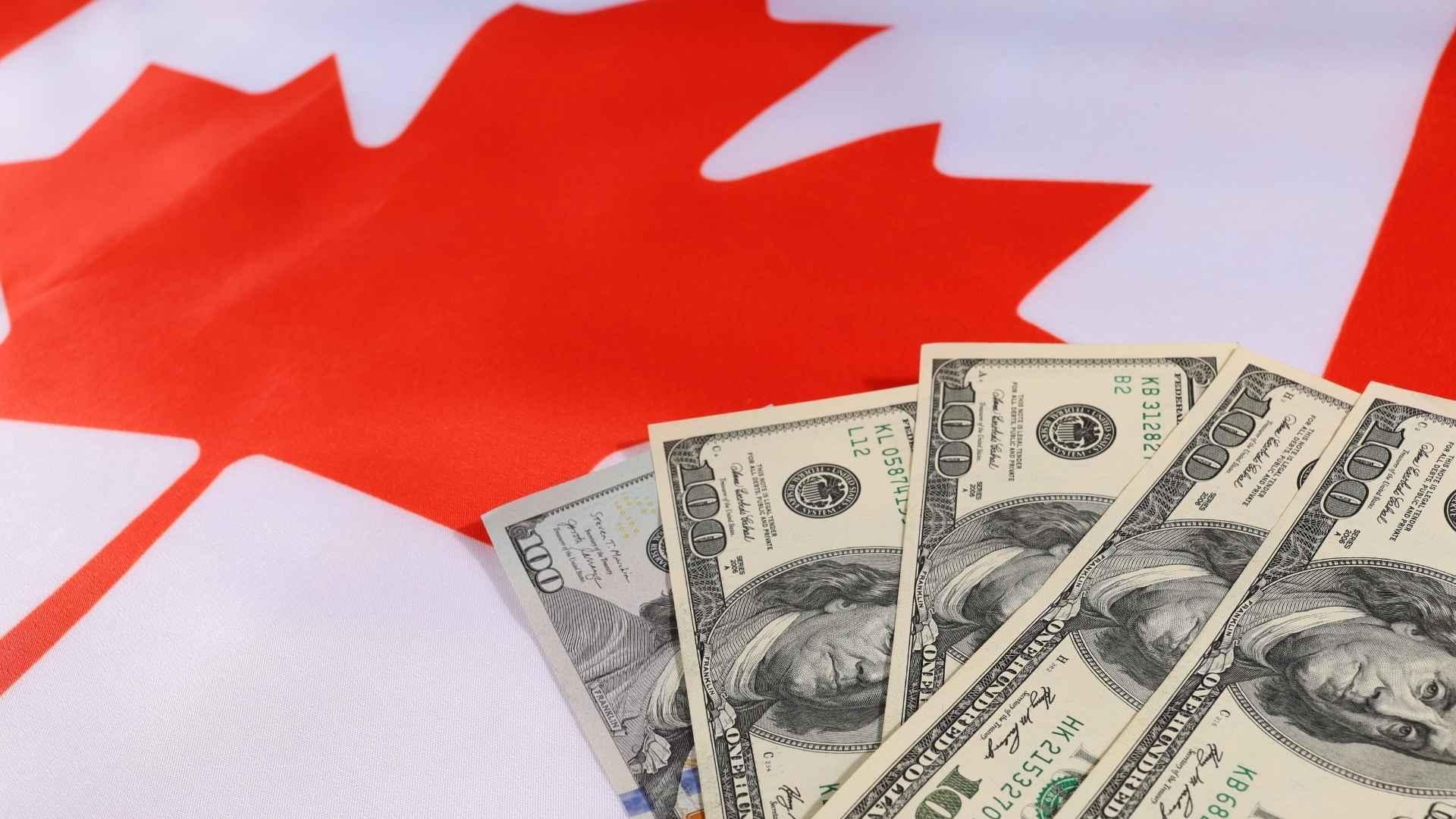 US one hundred dollar bills fanned over a Canadian flag